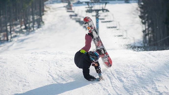 A snowboarder holds out their hands while falling on a ski slope